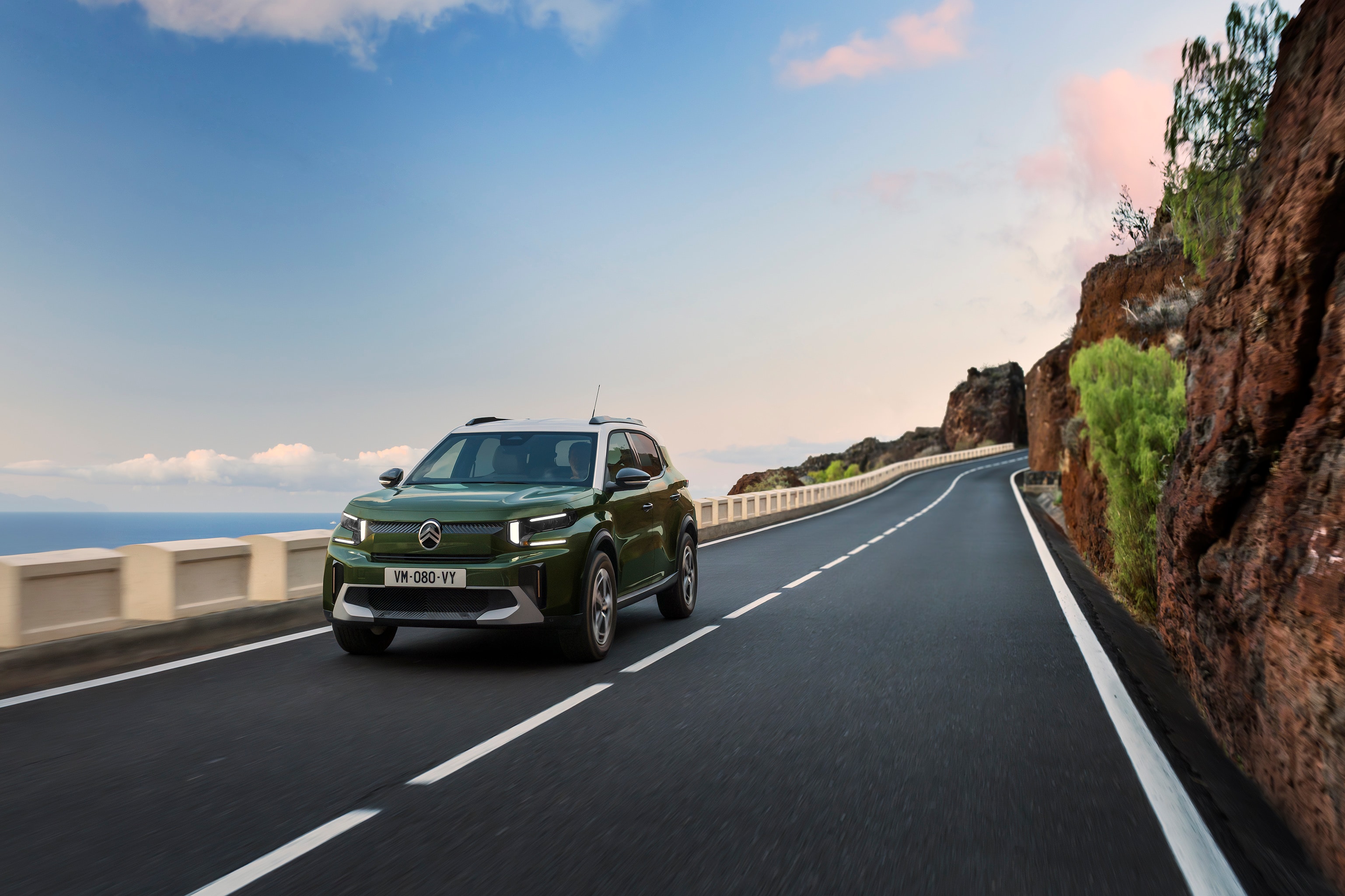 Front three‑quarter driving view of Citroën ë-C3 compact SUV on a scenic road highlighting agile, confident and affordable everyday mobility.