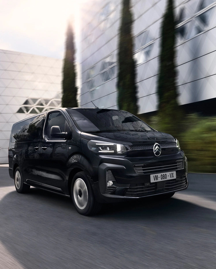 Front three‑quarter view of the Citroën ë‑SpaceTourer driving in an urban area, highlighting its modern electric design