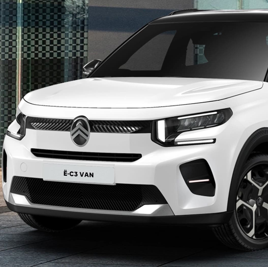 Front three-quarter view of the Citroën ë-C3 Van parked in an urban setting, highlighting its modern design and compact proportions.